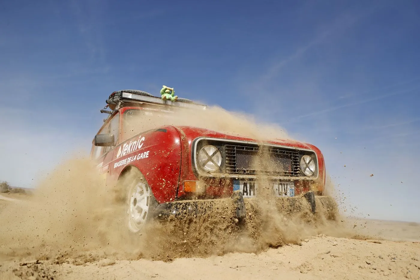 Une Renault 4L rouge soulève une gerbe de sable dans le désert marocain